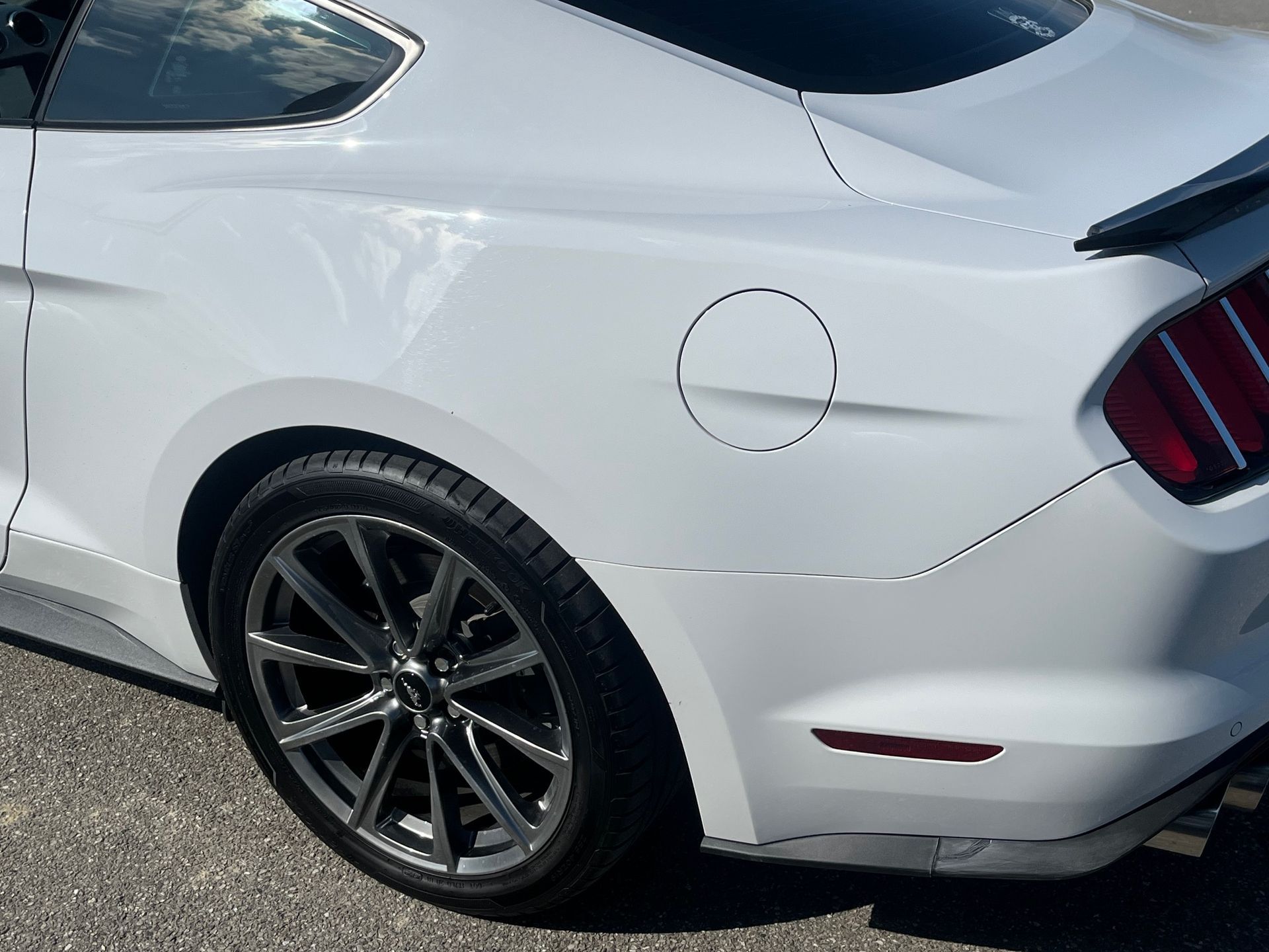 Vue arrière d'une voiture de sport blanche avec des jantes noires et une trappe à carburant visible.