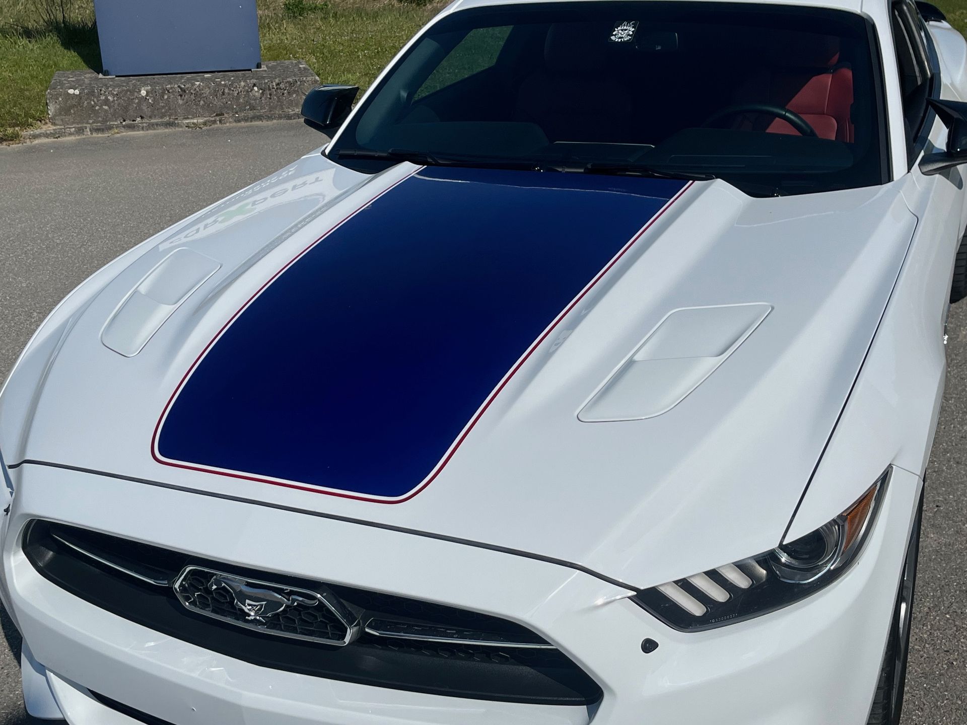 Voiture de sport blanche avec une bande bleu foncé sur le capot, garée à l'extérieur