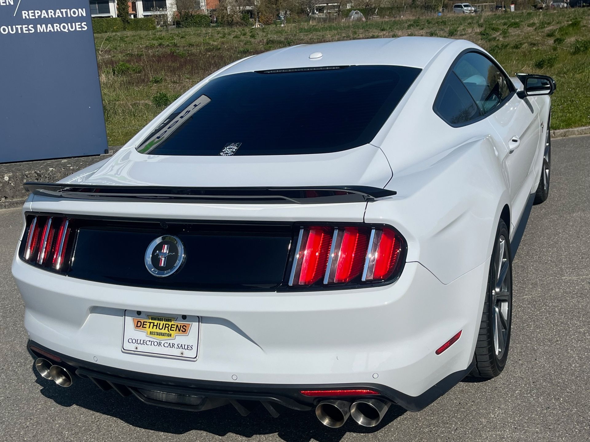 Coupé sport blanc vu de l'arrière, stationné sur le trottoir, vitres teintées foncées et feux arrière rouges.