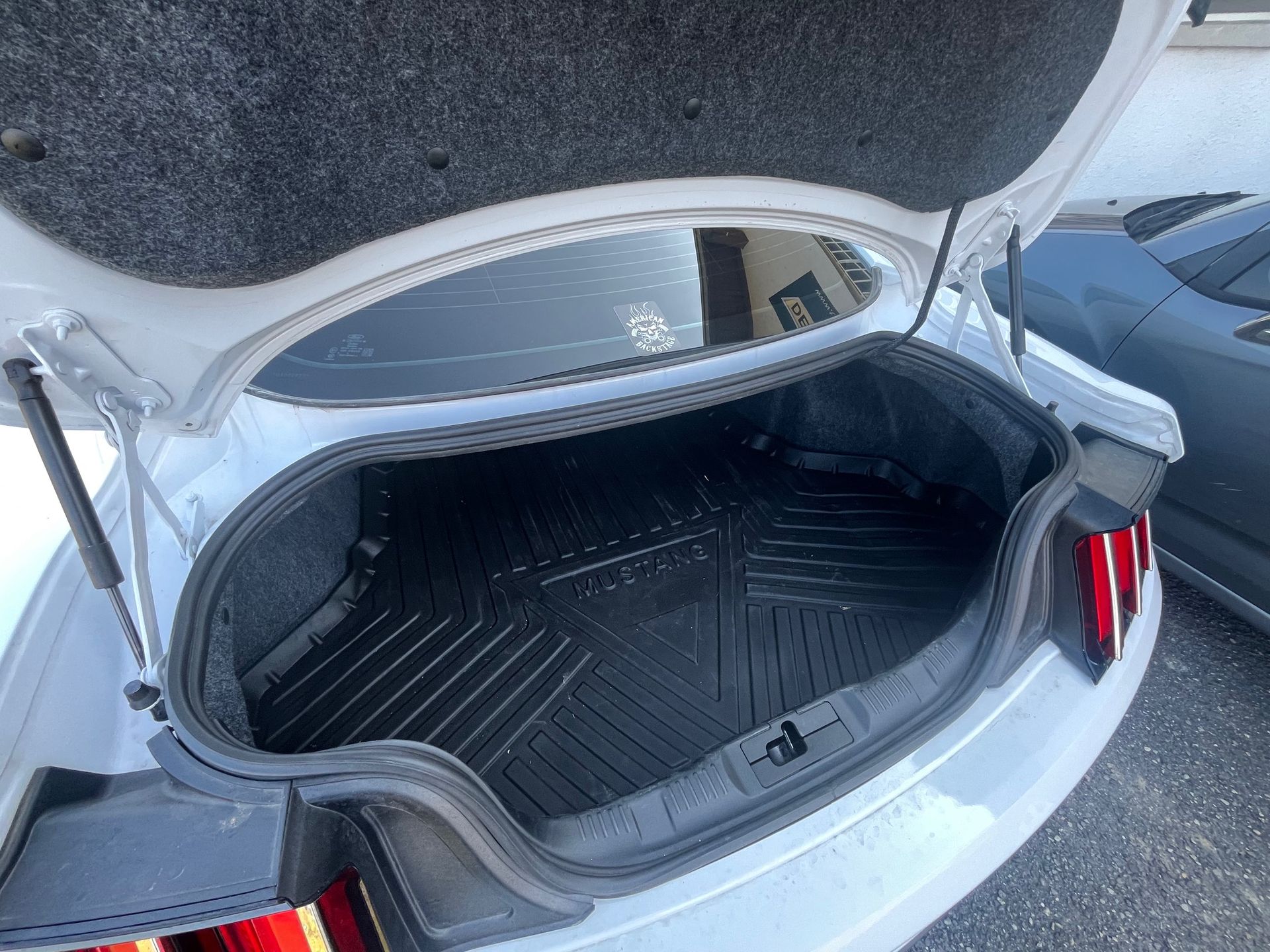 Coffre de voiture ouvert avec tapis de coffre noir et intérieur gris sur un parking