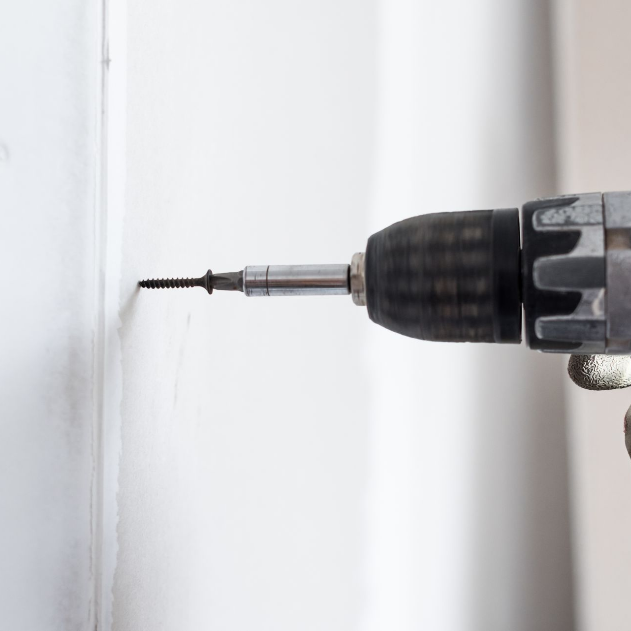 Perceuse enfonçant une vis dans un mur blanc