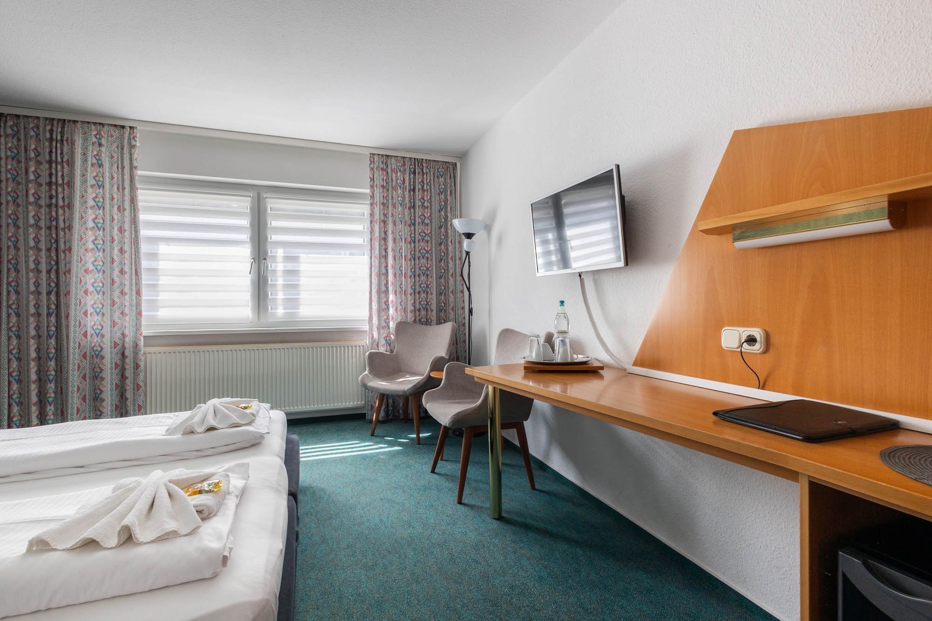 Ein Hotelzimmer mit zwei Betten, einem Schreibtisch, Stühlen und einem Fernseher.