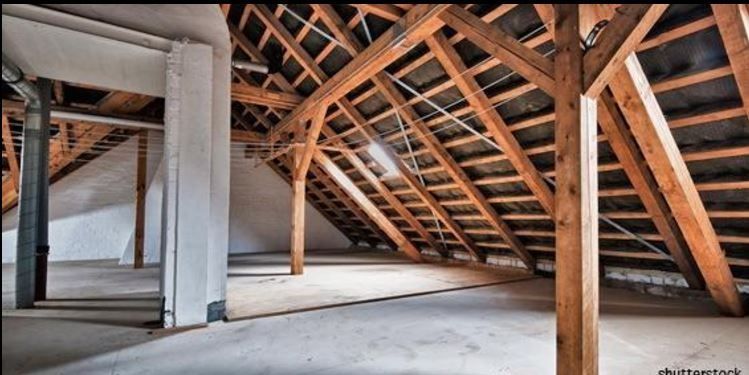 Intérieur du grenier avec charpente apparente, plancher non fini et structure de toit en pente