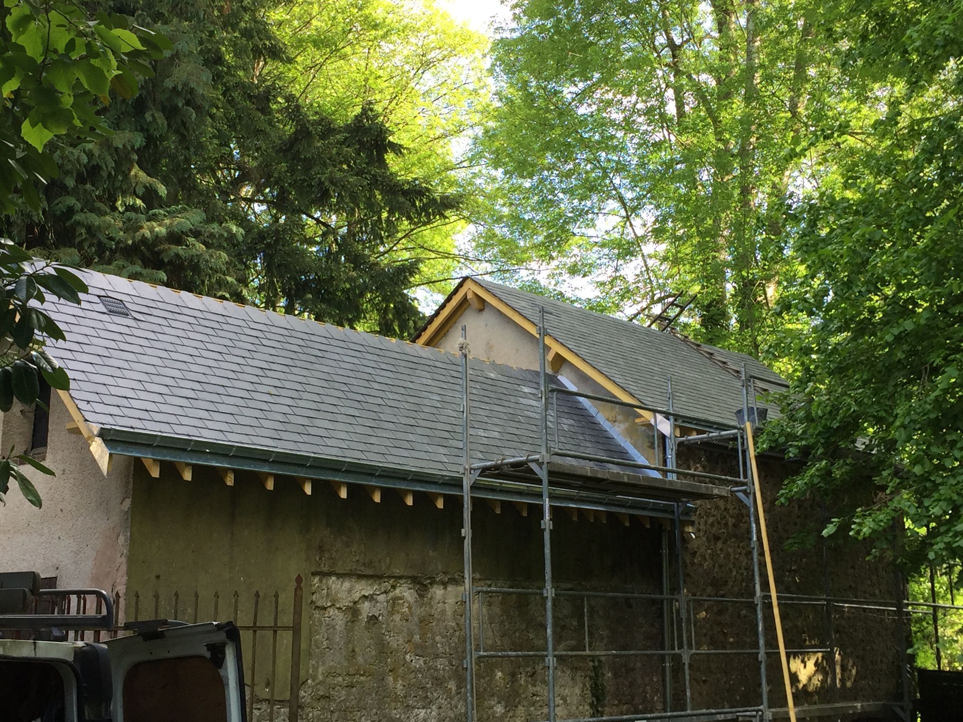 Toiture de maison en réparation avec des échafaudages, entourée d'une dense végétation.