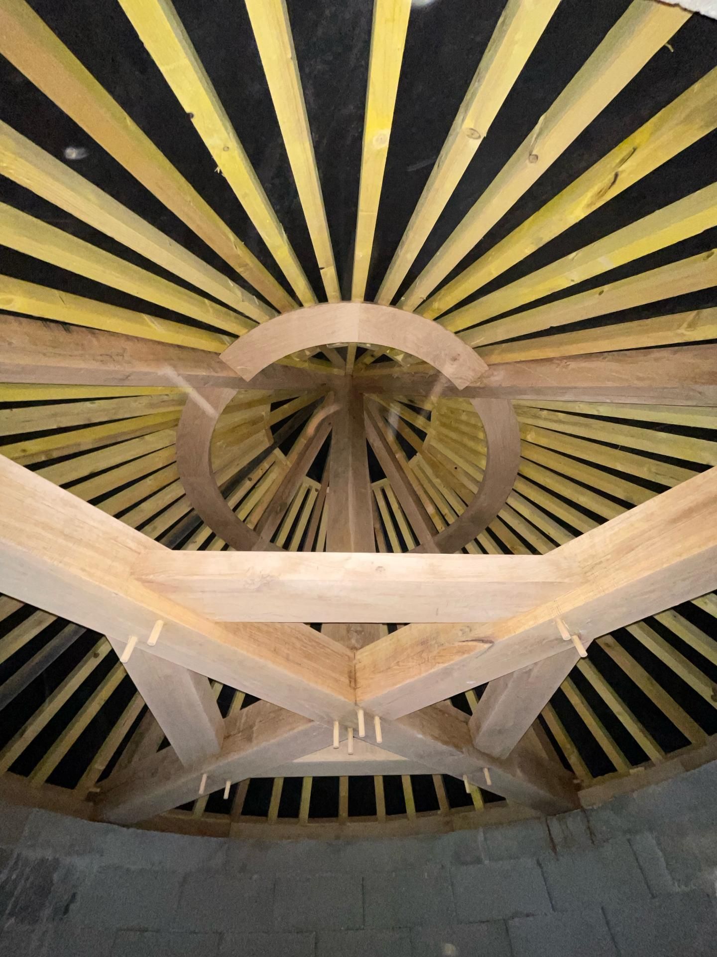 Structure de plafond radiale en bois avec des poutres convergeant autour d'une ouverture circulaire centrale