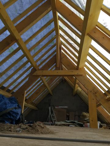 Grenier en construction avec charpente en bois, fenêtres de toit et matériaux de construction au sol