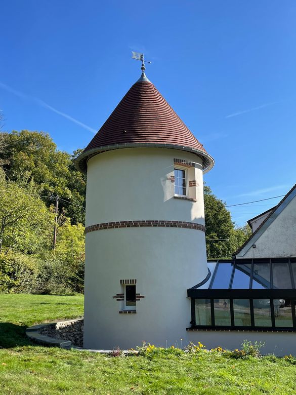 Tour ronde blanche coiffée d’un toit conique rouge, à côté d’un bâtiment au toit vitré, sous un ciel bleu.