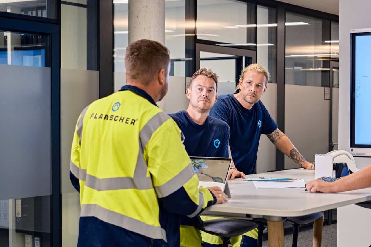 A close-up of a black 360-degree camera with two lenses and antennas, positioned near a person wearing a hard hat and vest.