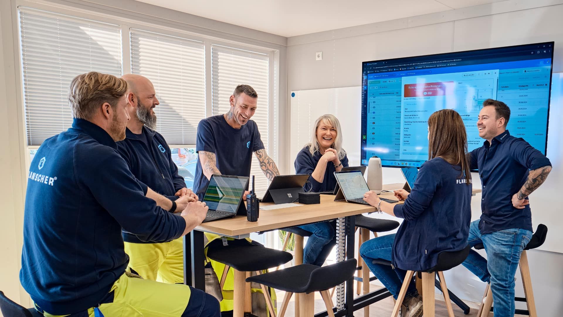Group of people in blue shirts in front of a brick building; sign with blue logo.
