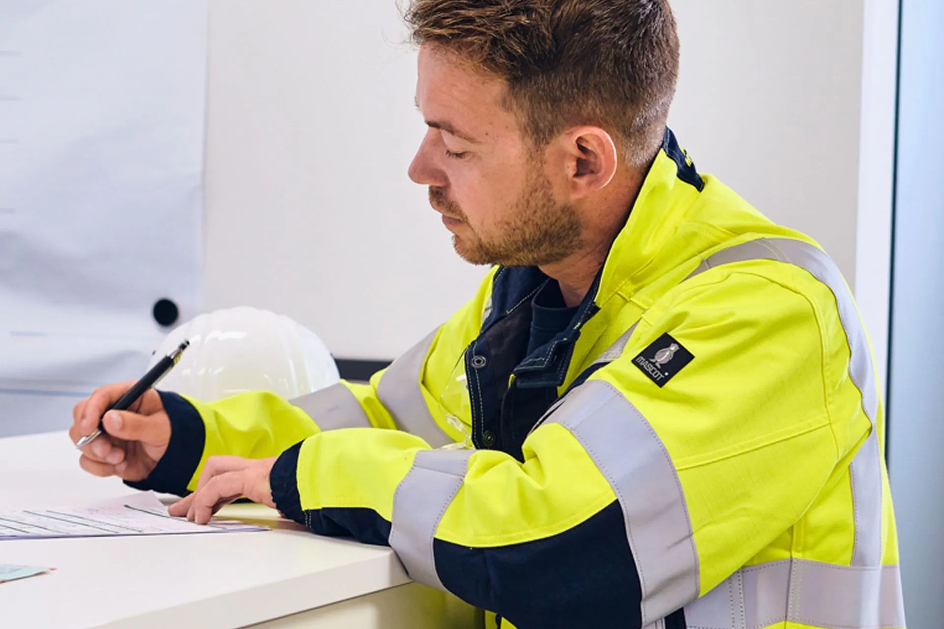 Man holding drone, looking at it, with monitors displaying aerial views, sitting at a desk.