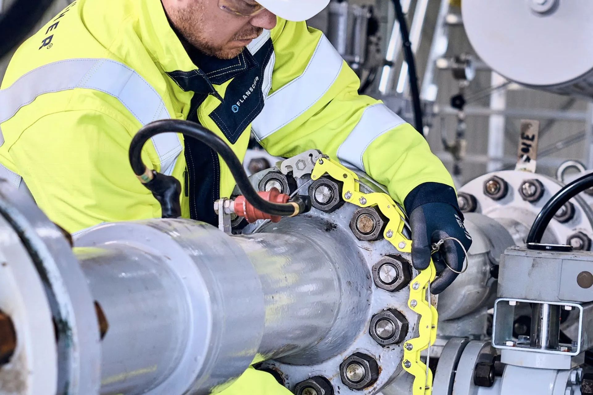 Man holding drone, looking at it, with monitors displaying aerial views, sitting at a desk.