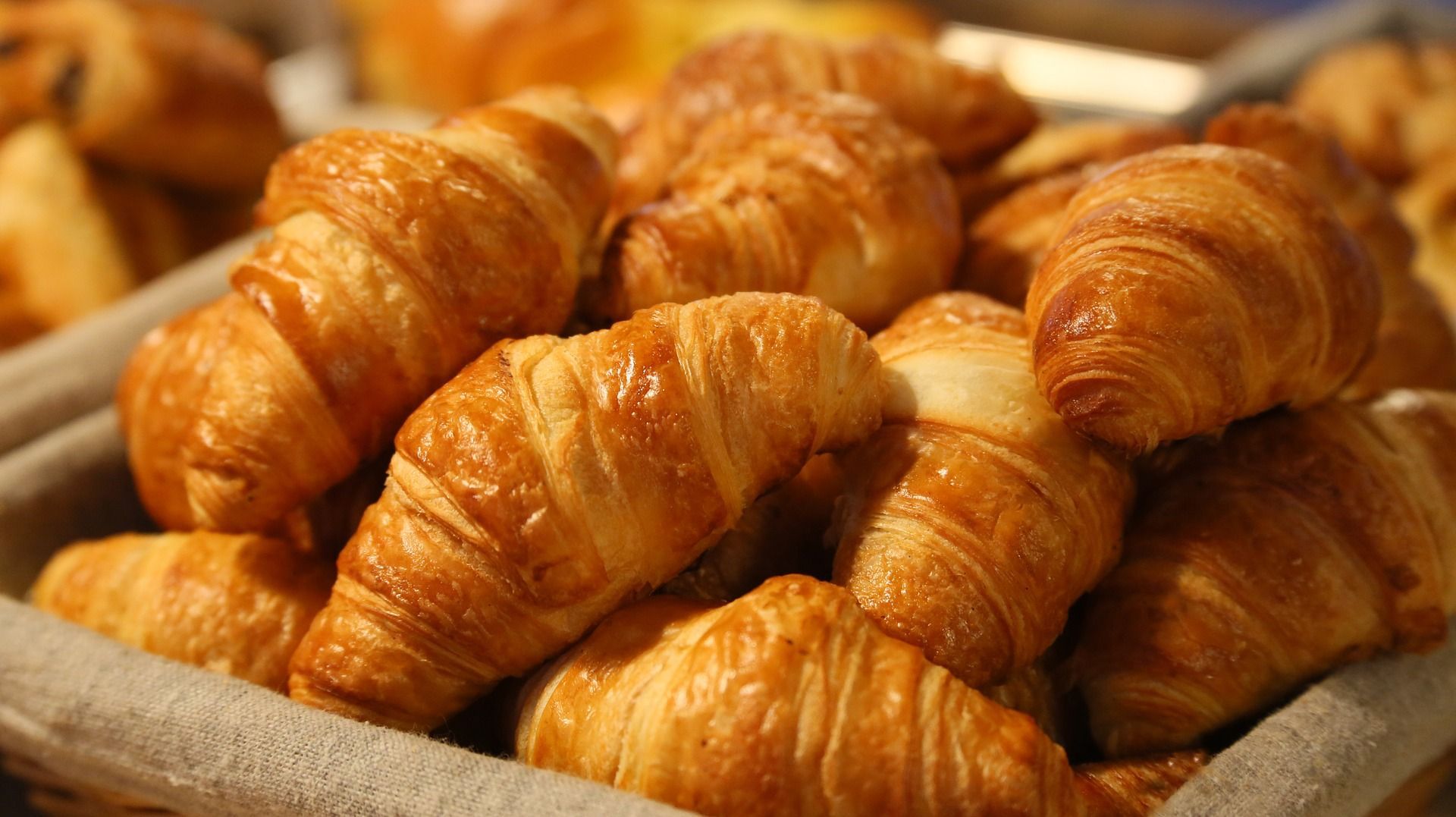 Close-up of freshly baked golden croissants stacked in a basket, showing flaky, buttery layers and a crisp, glossy crust.