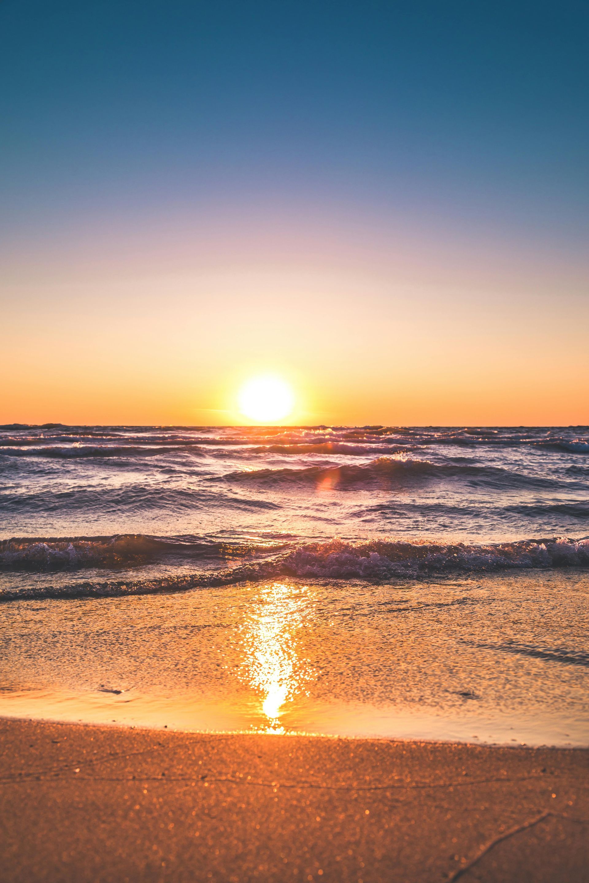 Golden sunset over the ocean, with the sun low on the horizon casting warm orange and yellow light across rolling waves and reflecting on the water’s surface.