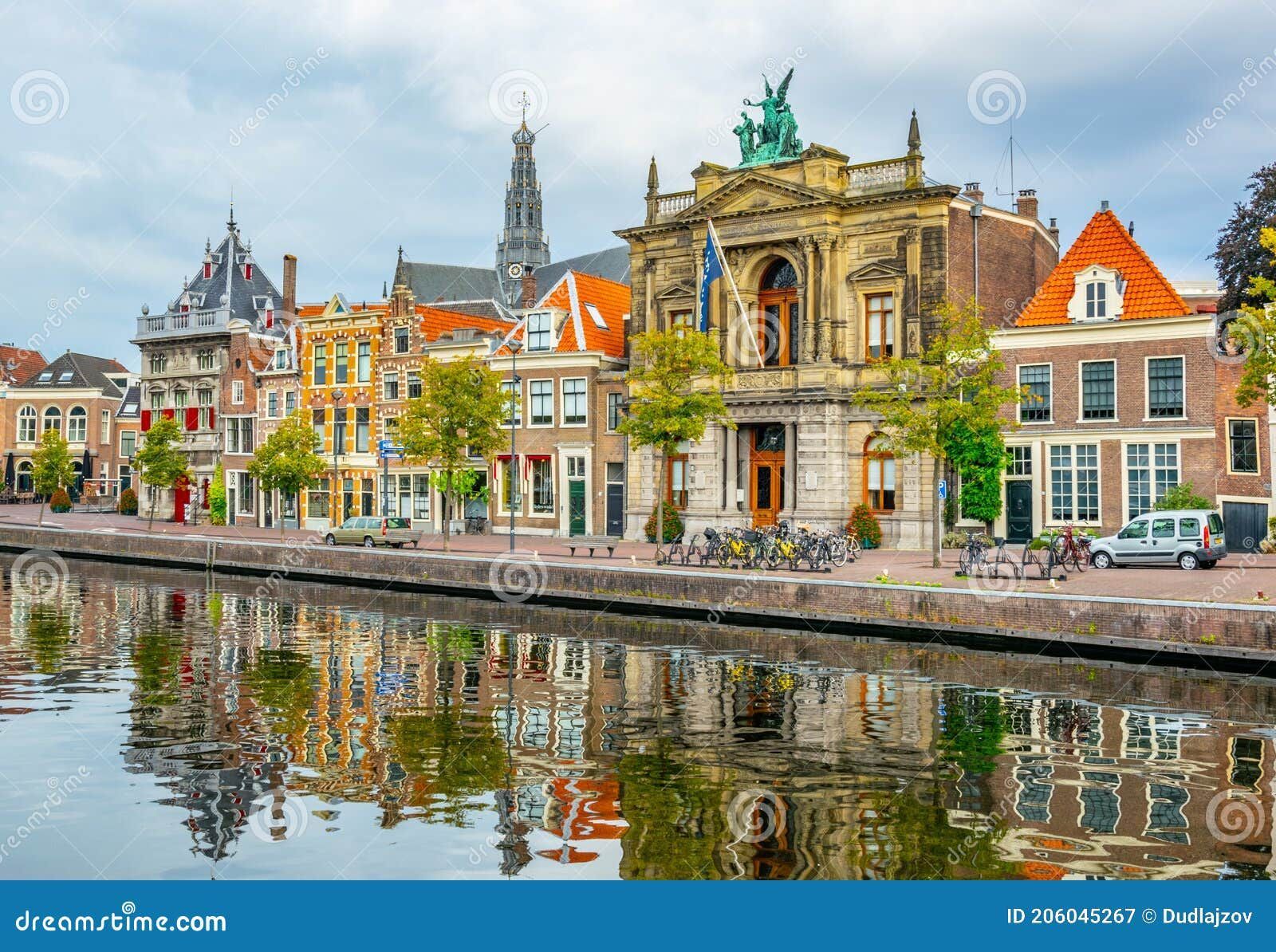 Historic canal in Haarlem with colorful gabled houses, a grand classical building, bicycles along the quay, and reflections shimmering in the calm water.