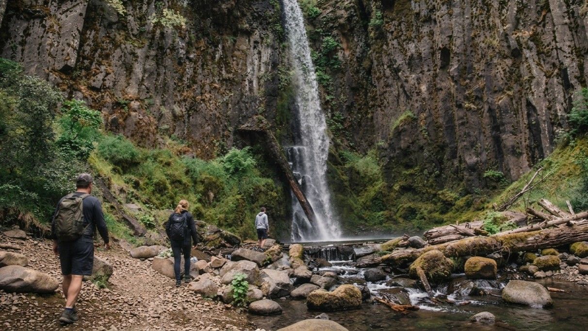 Hikers in a rocky gorge near a tall waterfall beside a stream
