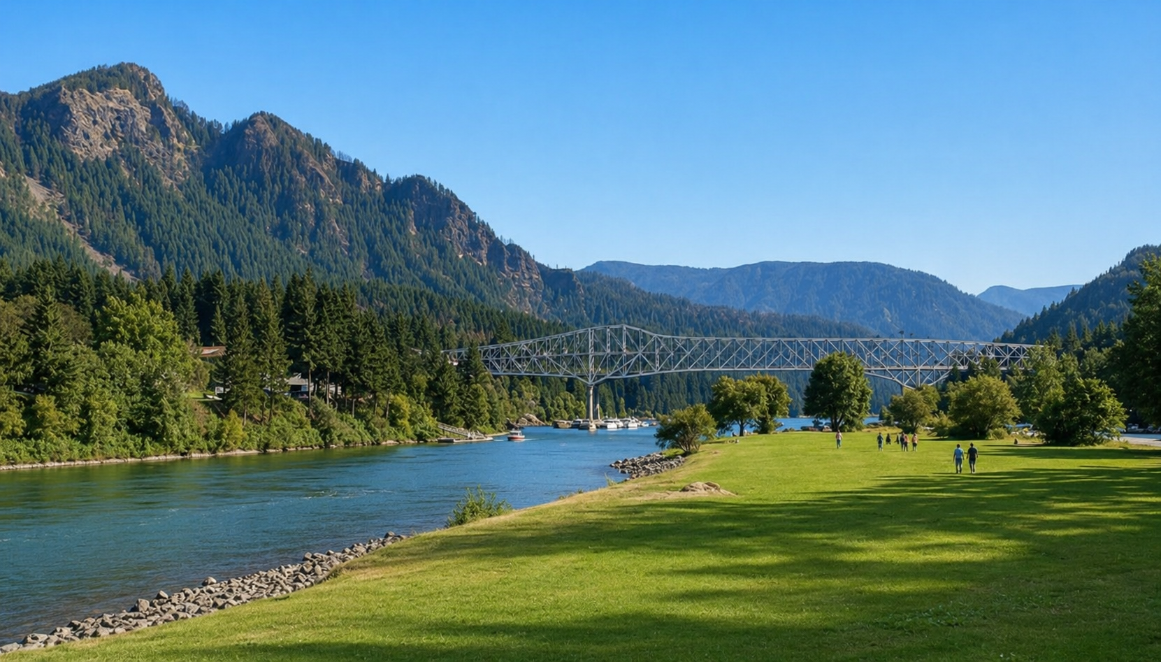 Scenic river valley with green meadow, forested mountains, and a bridge under a clear blue sky