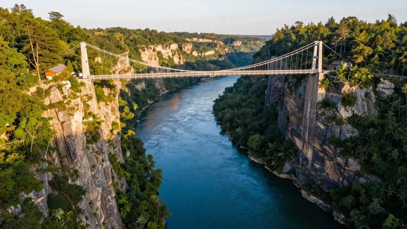 Suspension bridge over a deep blue river gorge, surrounded by rocky cliffs and green trees at sunset