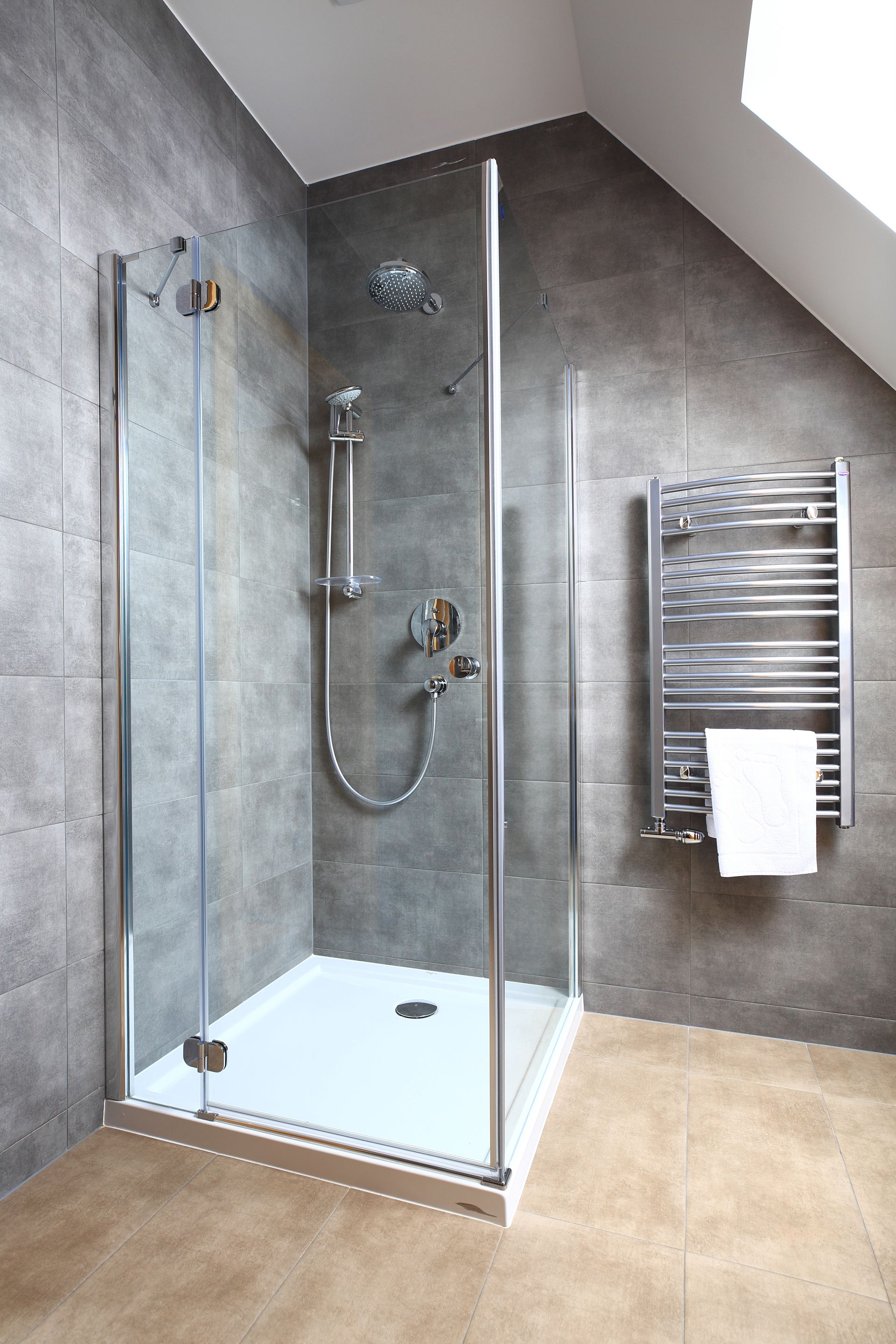 Une cabine de douche moderne avec des murs carrelés gris, une porte en verre, une robinetterie argentée et un sèche-serviettes mural.