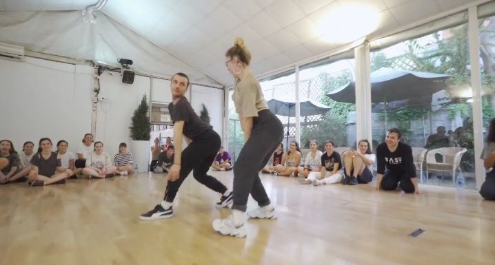 Un grupo de personas está sentado en el suelo mirando a una pareja bailar en una habitación.