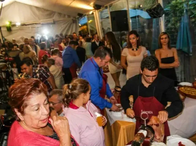 Un grupo de personas se reúne alrededor de una mesa donde un hombre está cortando carne.