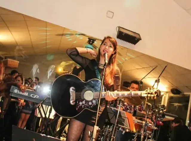 Una mujer cantando en un micrófono mientras sostiene una guitarra.