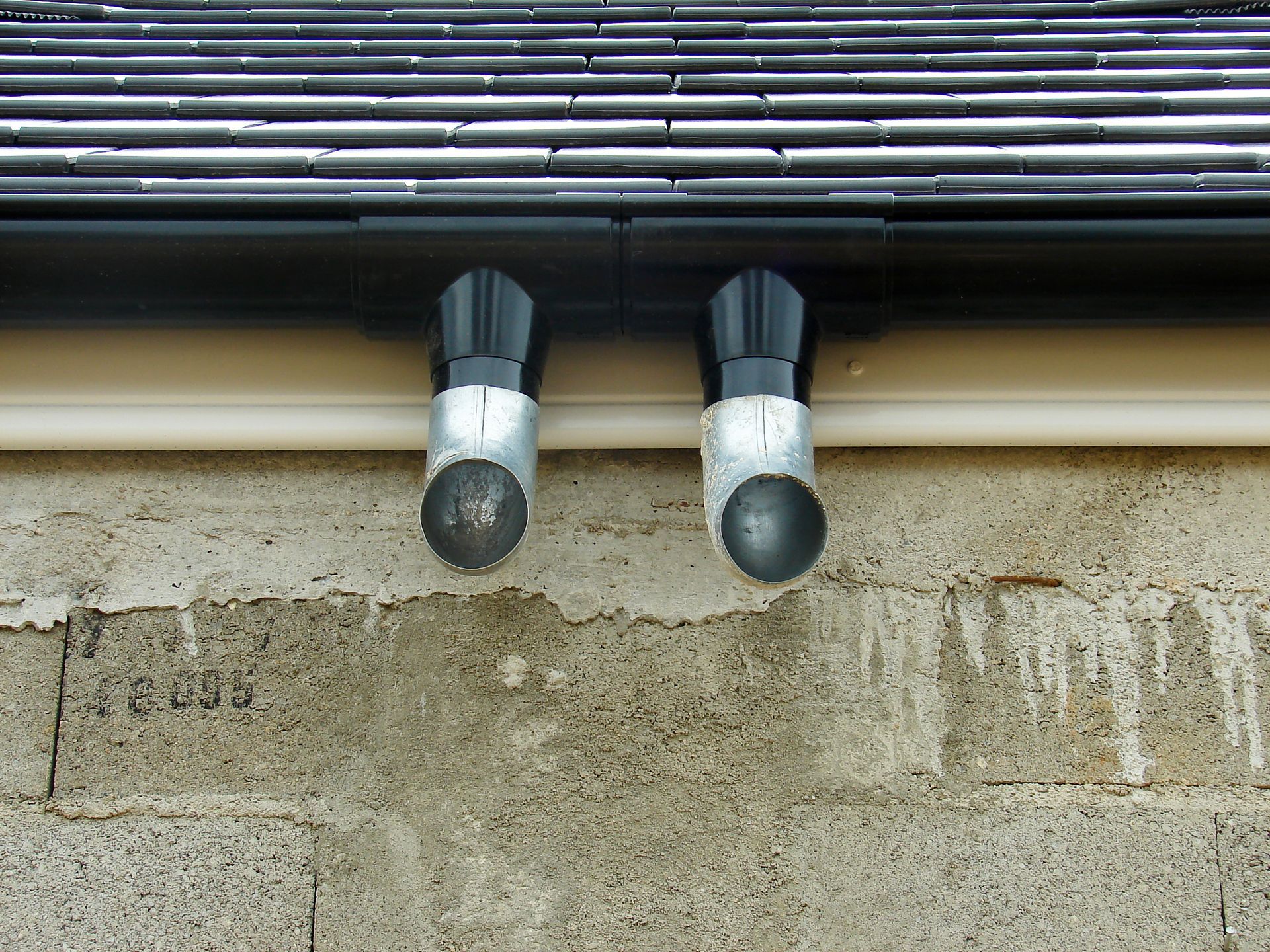 Toit sombre percé de puits de lumière, cheminée et antenne parabolique se détachant sur un ciel bleu azur. Façade blanche du bâtiment en contrebas.