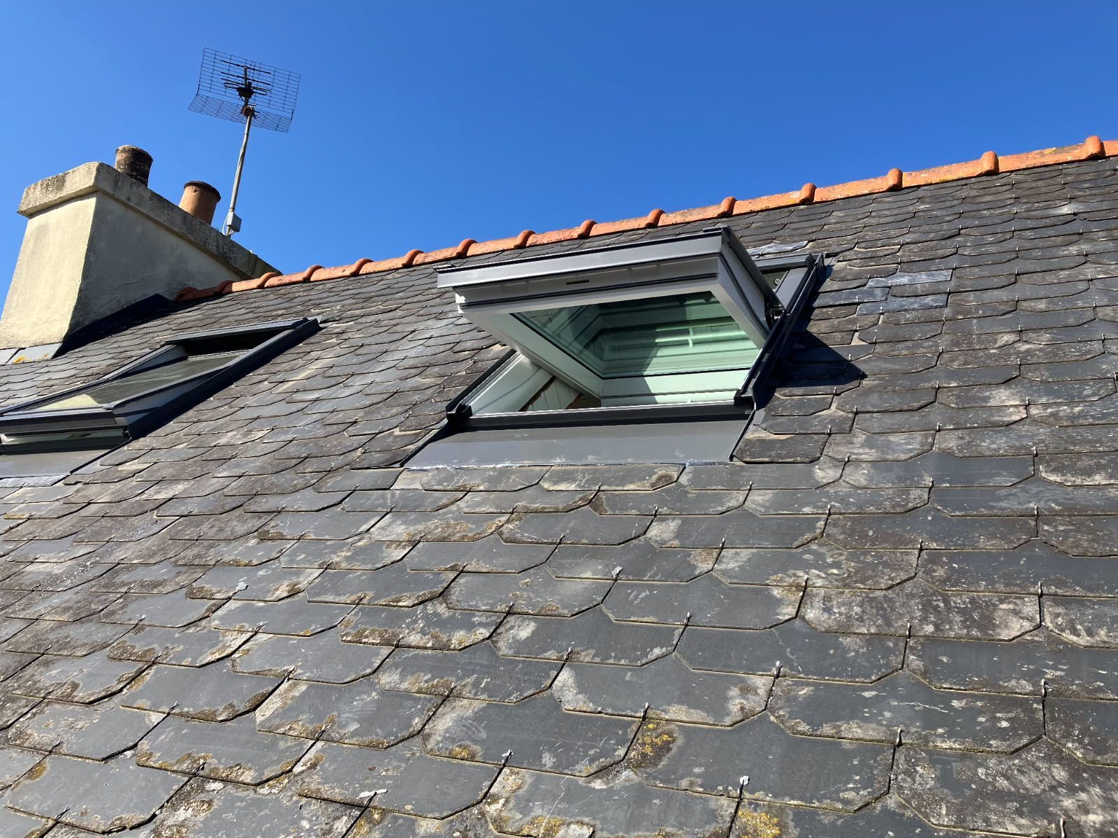 Toit en ardoise avec puits de lumière ouvert ; ciel bleu en arrière-plan.