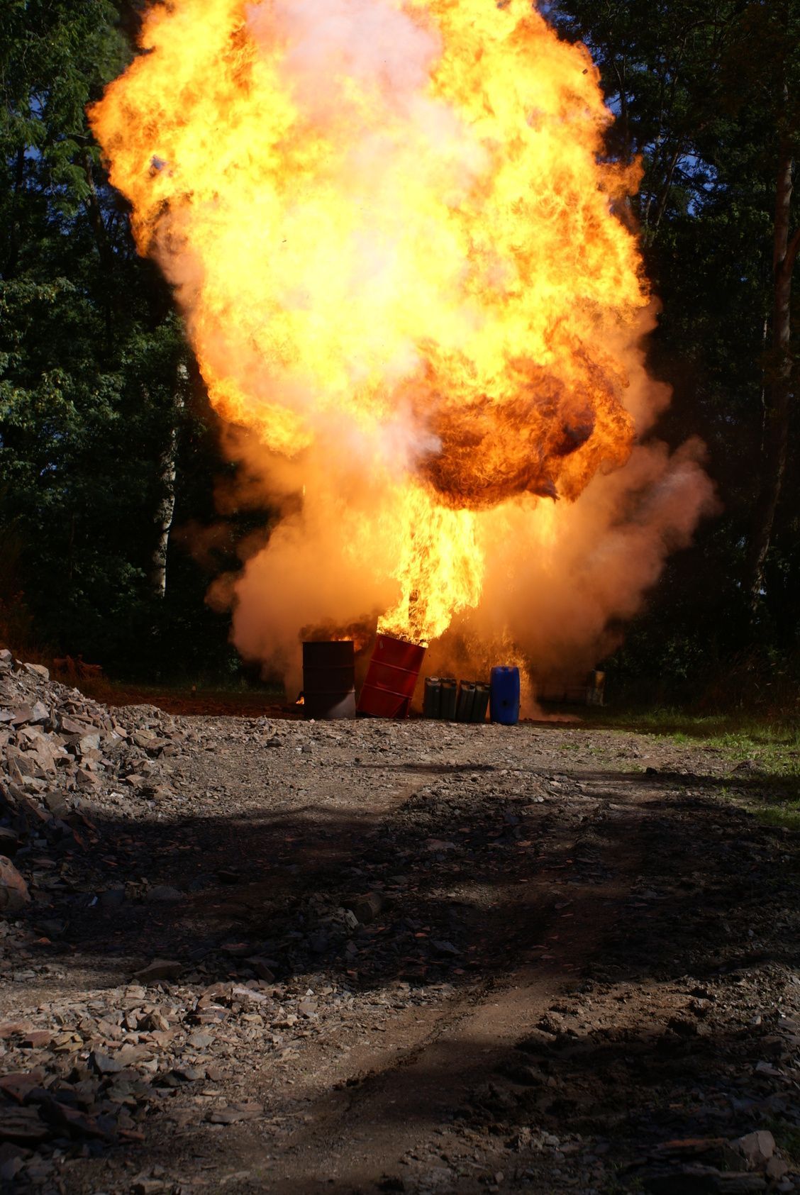 Ein Feuerwehrmann auf einer Drehleiter spritzt Wasser auf einen riesigen, hellorangefarbenen Feuerball, der in den dunklen Himmel aufsteigt.