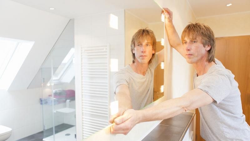 Ein Mann betrachtet sein Spiegelbild in einem Badezimmerspiegel.