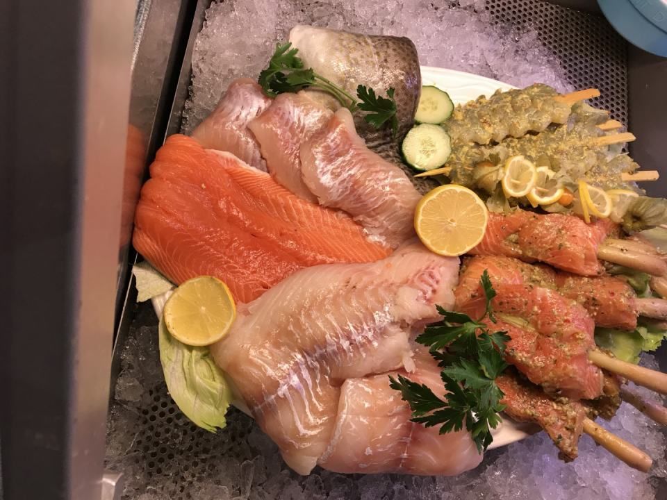 Auswahl an frischen Fischfilets und Spießen auf Eis, garniert mit Zitrone und Petersilie.