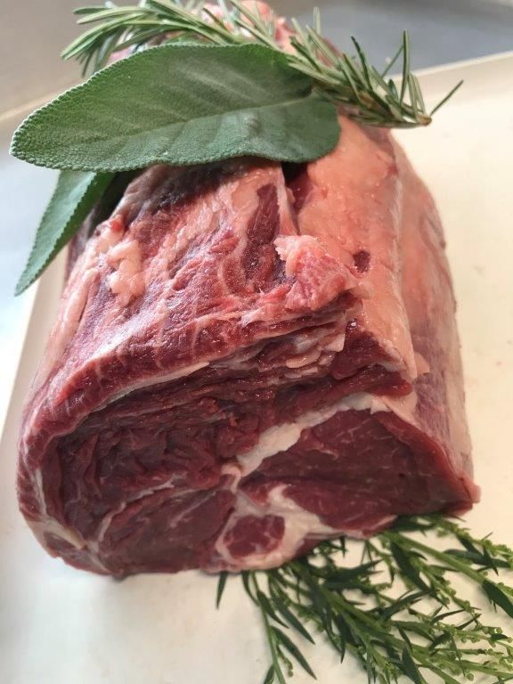 Roher Lammbraten mit Rosmarin- und Salbeigarnitur auf weißem Untergrund.