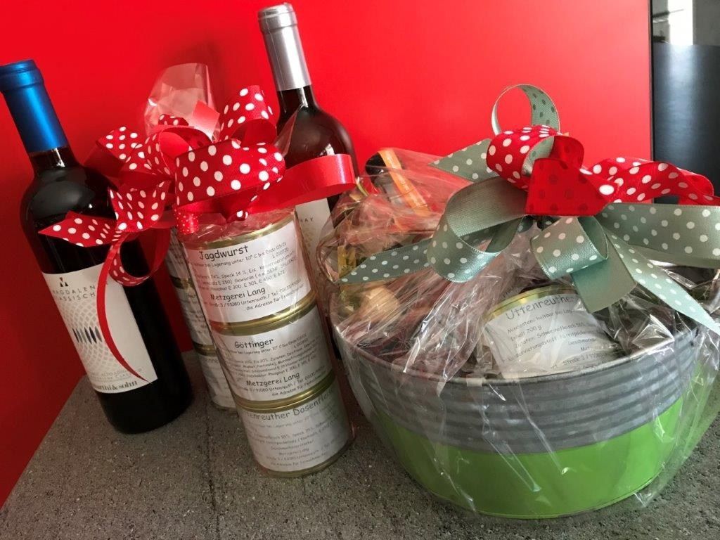 Geschenkkorb mit Weinflaschen, Gläsern und dekorativen Bändern, roten und grünen Akzenten.