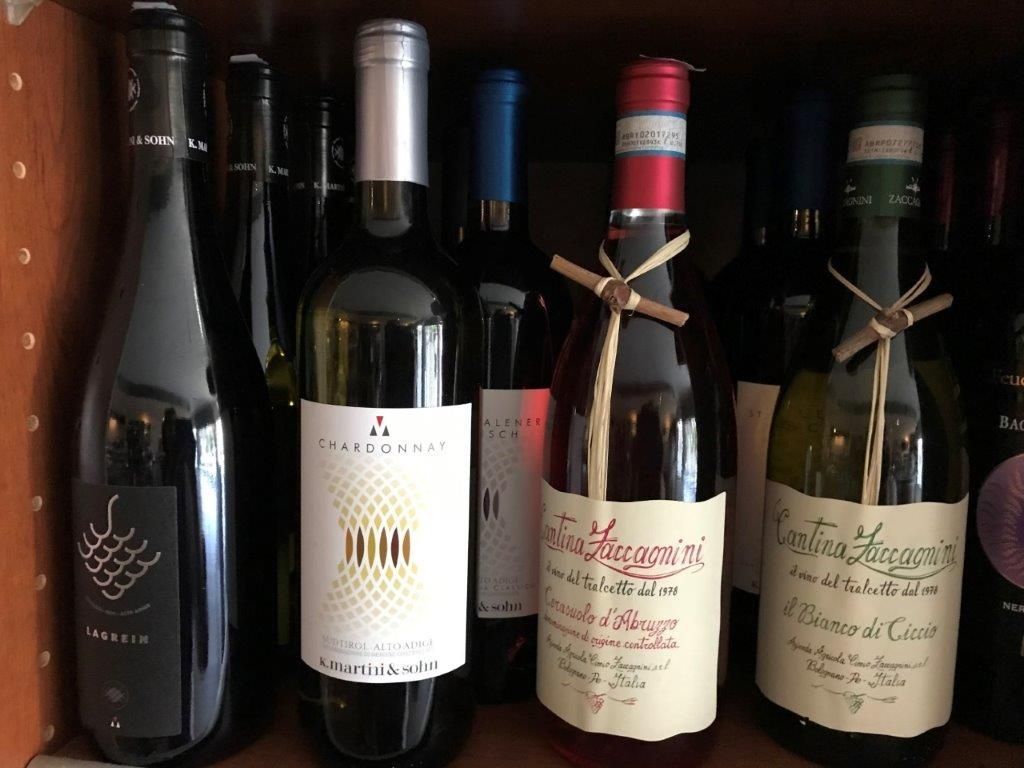 Weinflaschen im Regal, verschiedene Größen und Etiketten, einige mit Bindfäden um den Flaschenhals.