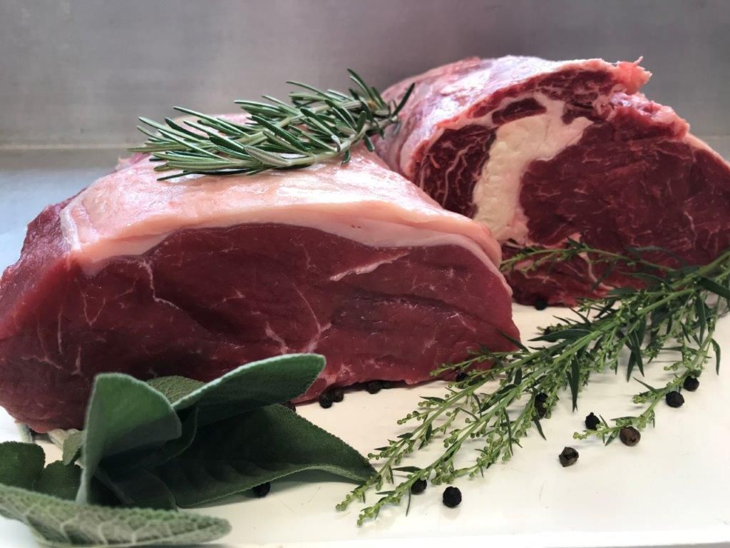 Zwei Stücke rohes rotes Fleisch, eines davon mit sichtbarem Fett, garniert mit Kräutern und Pfefferkörnern.