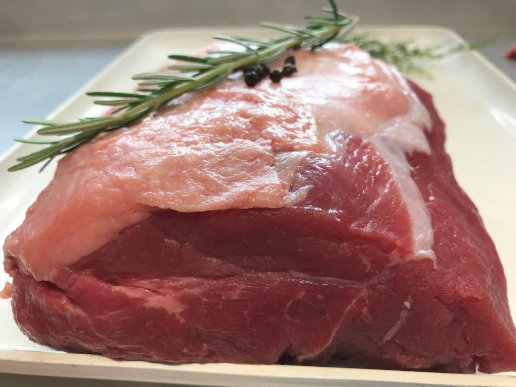 Roher Rinderbraten mit Fettschicht und Rosmarinzweig auf einer weißen Platte.