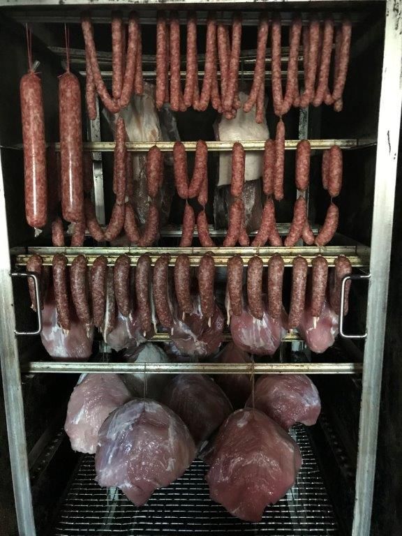 Geräucherte Würste und Fleisch hängen in einem Räucherofen.