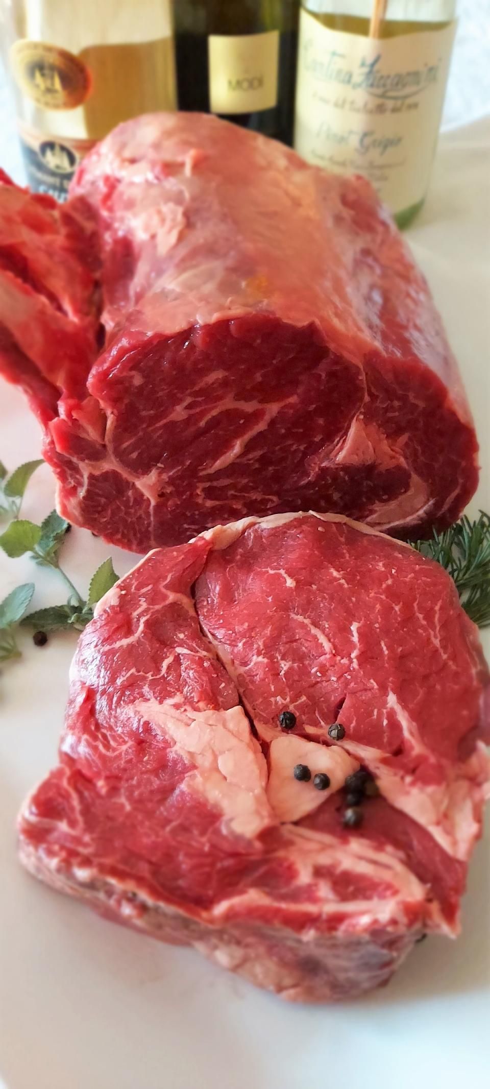 Roher Rinderbraten und Steak mit Pfefferkörnern, im Hintergrund Weinflaschen.