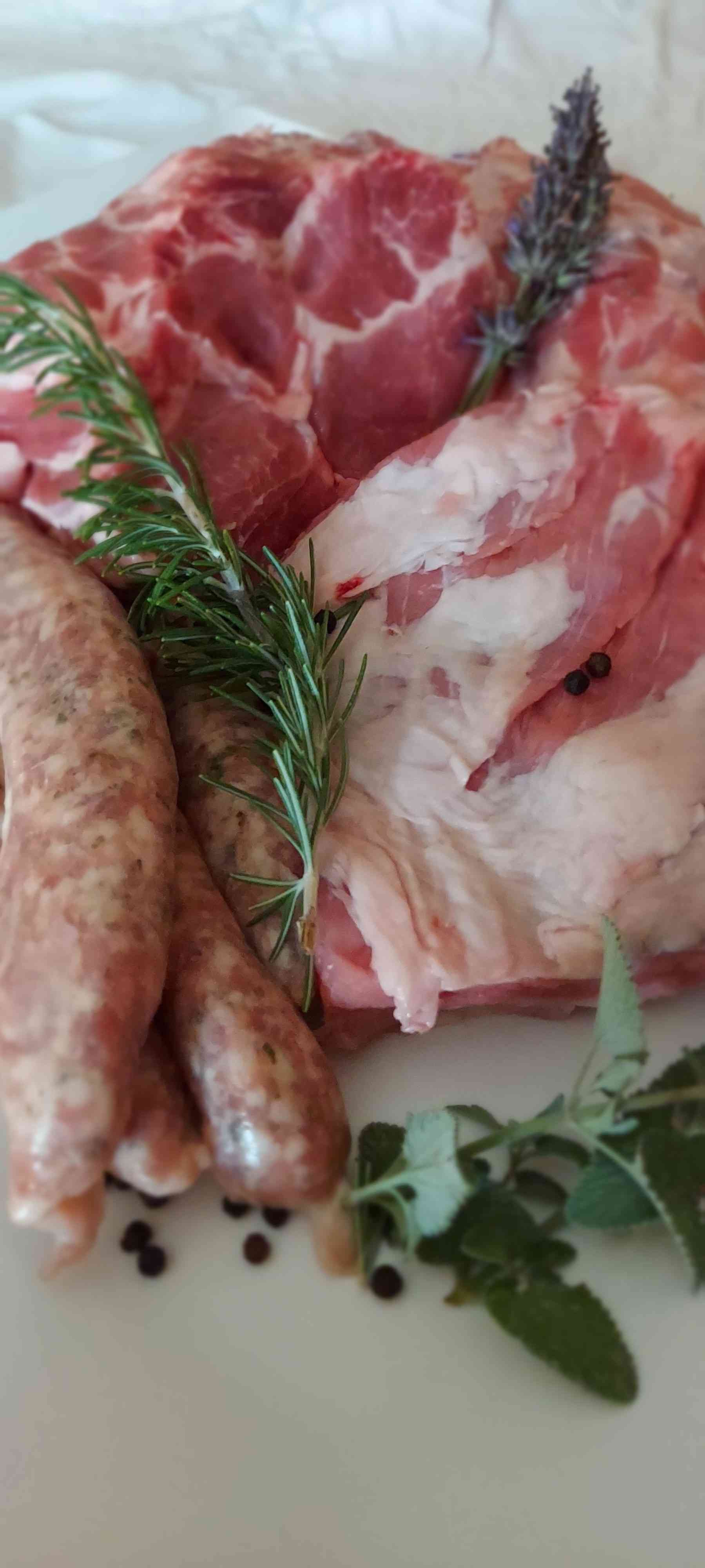 Rohes Schweinefleisch und Würstchen, garniert mit Kräutern und Pfefferkörnern, bereit zum Kochen.