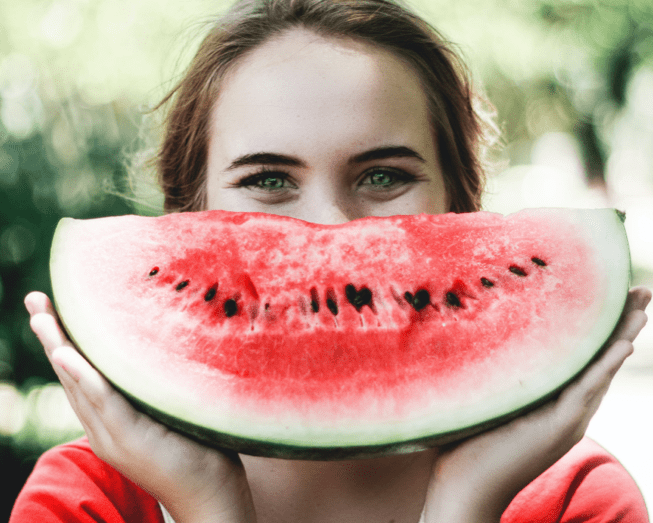Eine Frau hält eine Scheibe Wassermelone vor ihr Gesicht