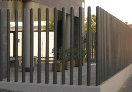 Casa moderna detrás de una valla vertical de listones oscuros en un muro de hormigón, con una planta en maceta visible en el interior.