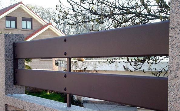 Una valla de madera marrón delante de una casa con árboles sin hojas detrás.