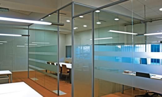 Interior de oficina moderno con paredes de vidrio, escritorios y mamparas esmeriladas.