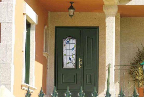 Porche delantero con puerta de entrada de color verde oscuro y panel de vidrio decorativo bajo una lámpara colgante.