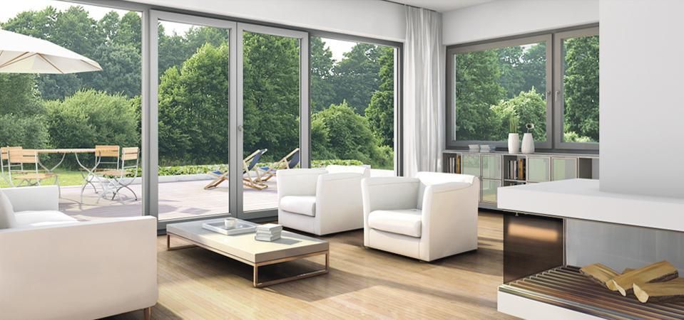 Luminoso salón moderno con sofás blancos, suelos de madera y grandes ventanales con vistas a zonas verdes.