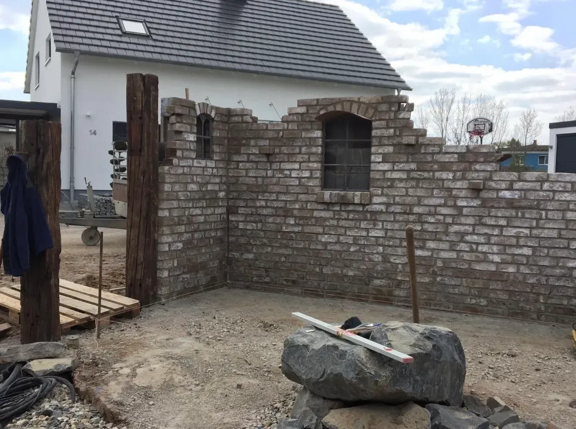 Vor einem Haus wird eine Ziegelmauer gebaut.