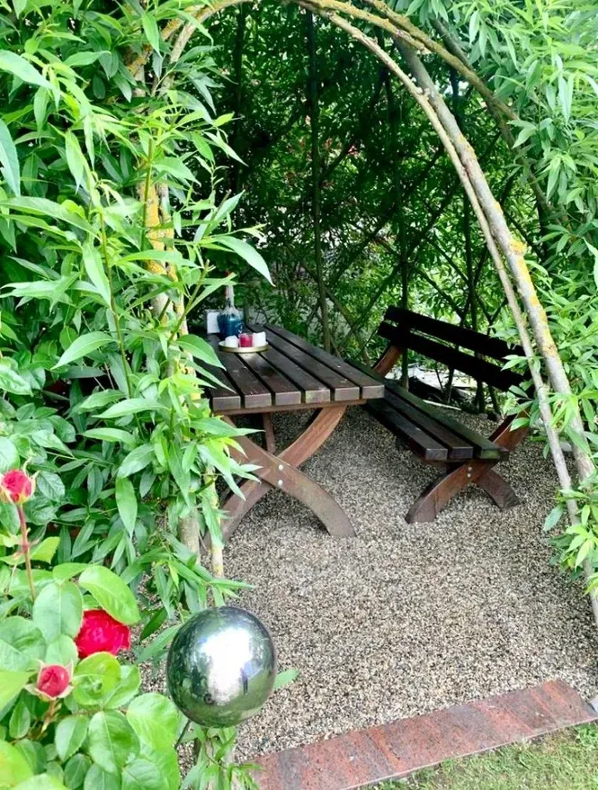 Ein Holztisch und Stühle stehen unter einem Baum in einem Garten.
