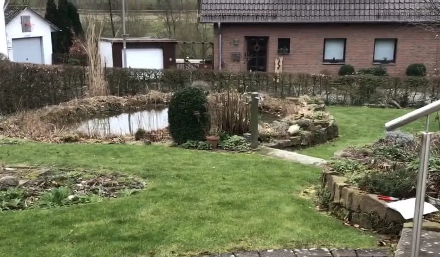 Ein üppiger grüner Rasen mit einem Teich in der Mitte vor einem Haus.