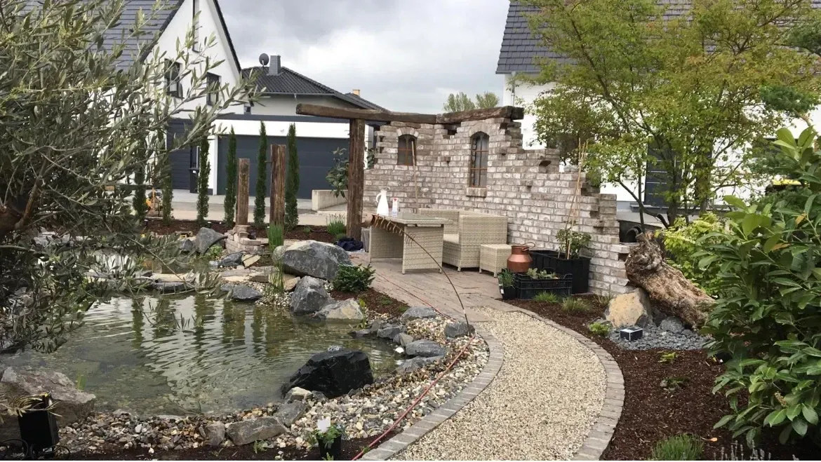 Inmitten eines Gartens vor einem Haus befindet sich ein Teich.