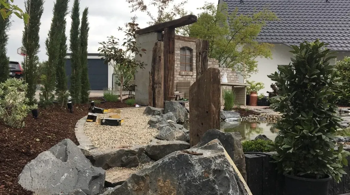 Ein Garten mit Felsen und Bäumen vor einem Haus.