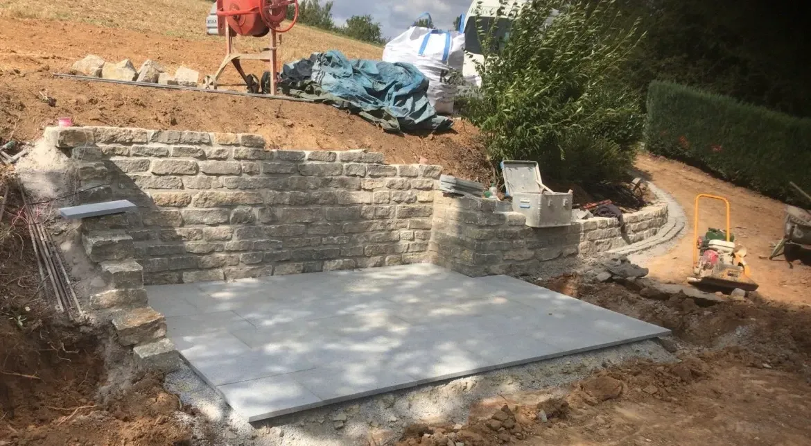 Eine Betonplatte liegt inmitten eines Feldes neben einer Backsteinmauer.